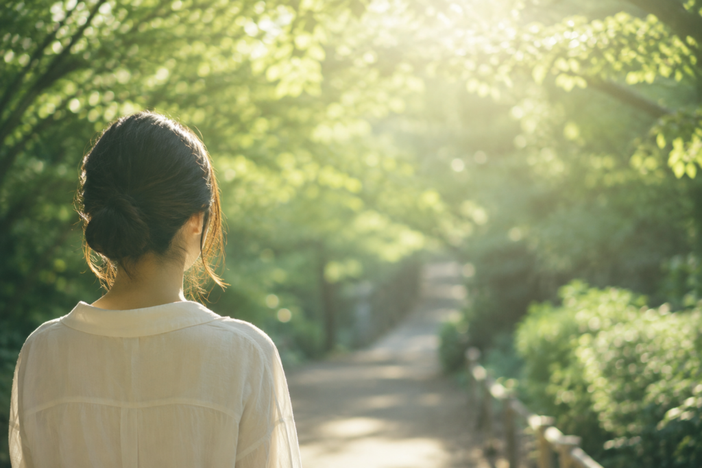 柔らかな光に包まれた森の中で、一人静かに立ち止まり、自分の内側へ意識を向ける人物の後ろ姿。